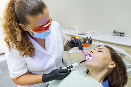 Dentist wearing protective goggles using blue light dental instrument on patient during sedation dentistry Astoria treatment