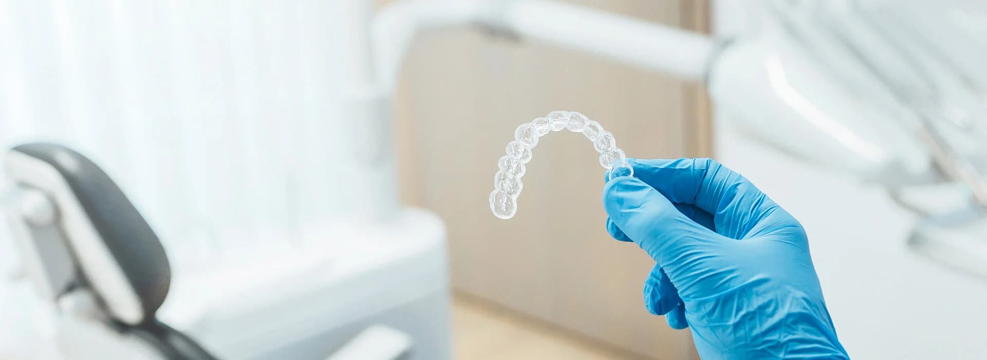 Photo of gloved hand holding aligner for is invisalign worth it consideration