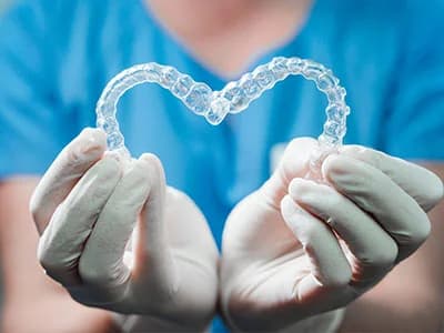 Photo of gloved hands holding aligners shaped like a heart for is invisalign worth it