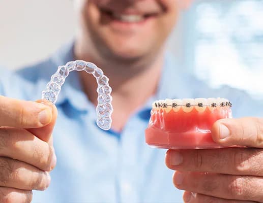 Photo of person holding a clear aligner and model with braces
