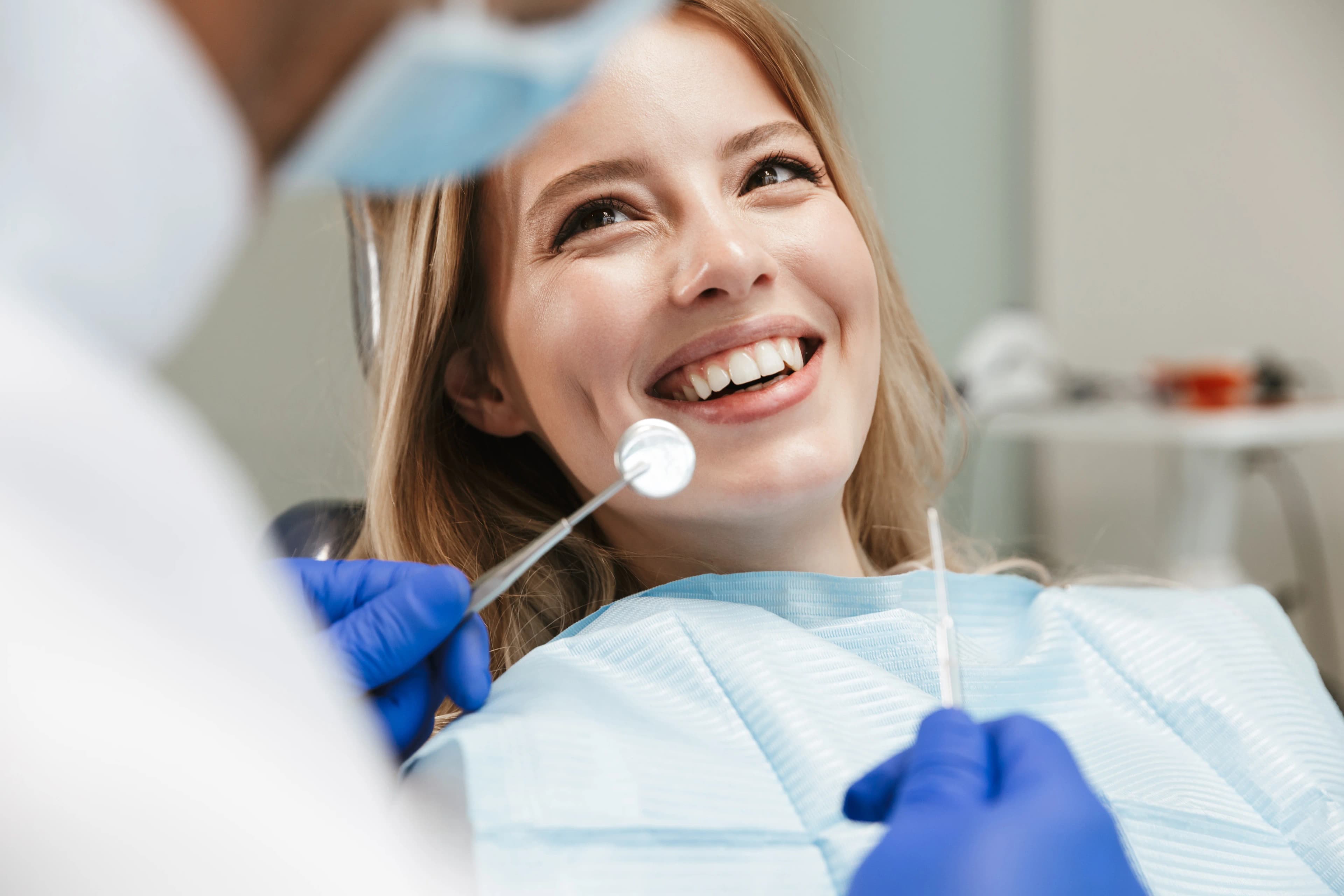 Photo woman smiling during teeth cleaning in Astoria with dentist holding dental instruments
