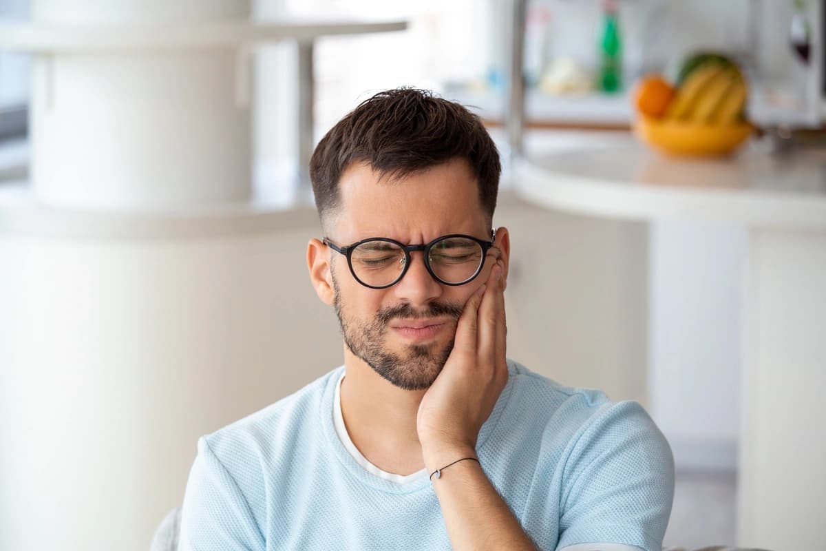 Man in light blue shirt and glasses holding cheek in pain eyes closed indicating toothache in need of affordable dental extractions
