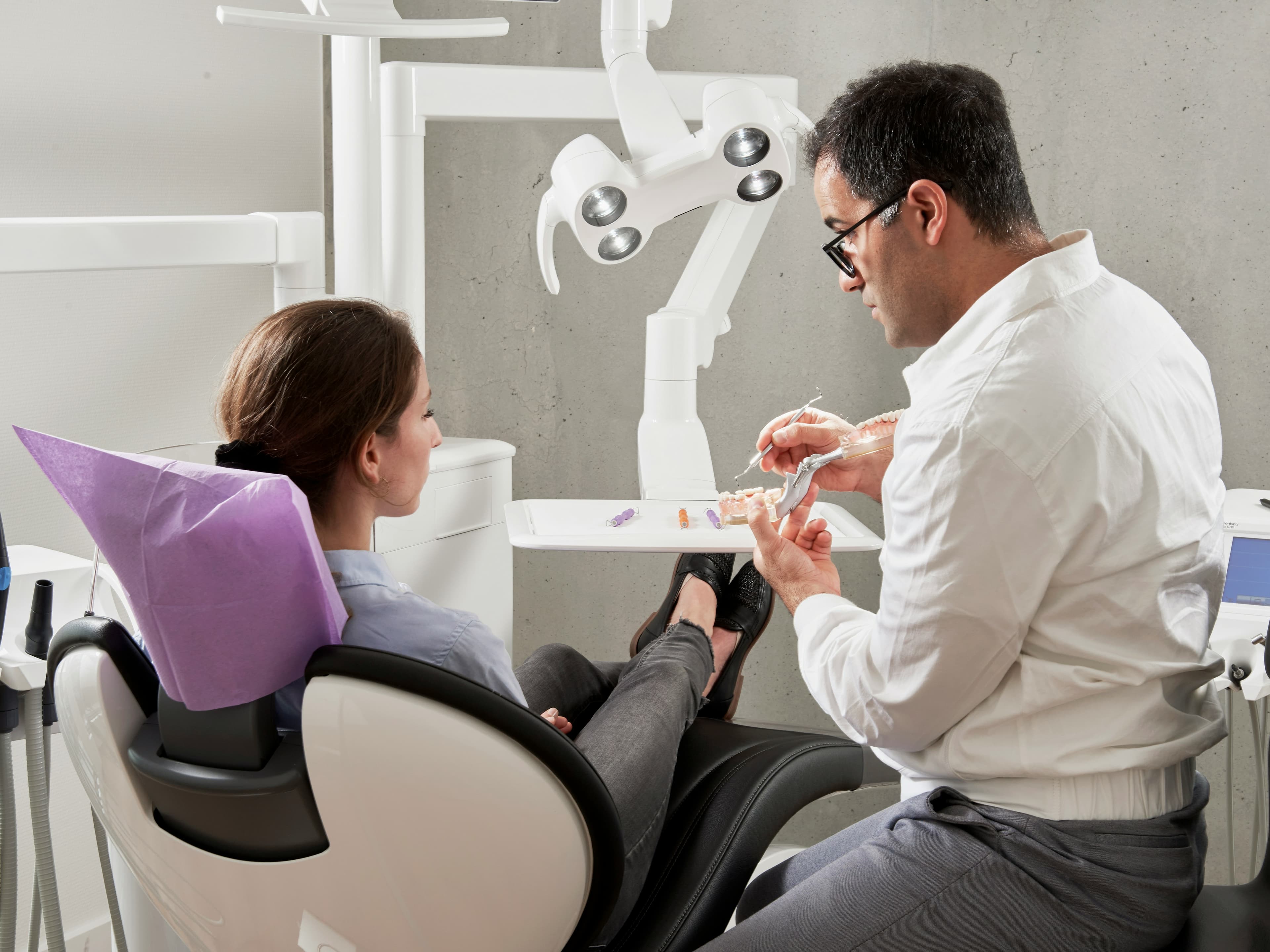 How Do They Do Dental Implants In One Day Dentist Showing Dental Model To Patient Seated In Dental Chair