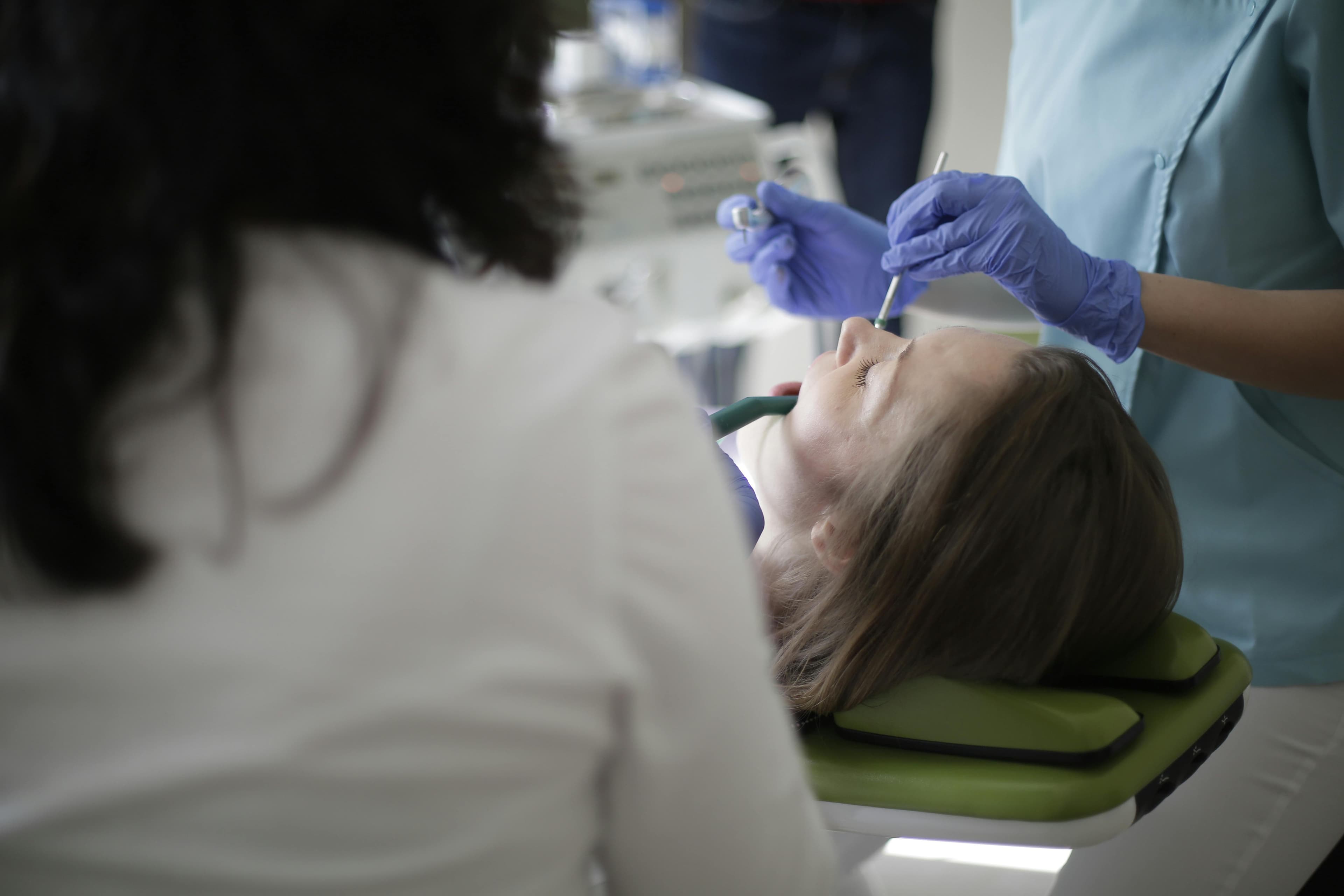 Dentist Wearing Gloves Treats Patient In Dental Chair Illustrating How Long Does A Dental Implant Procedure Take