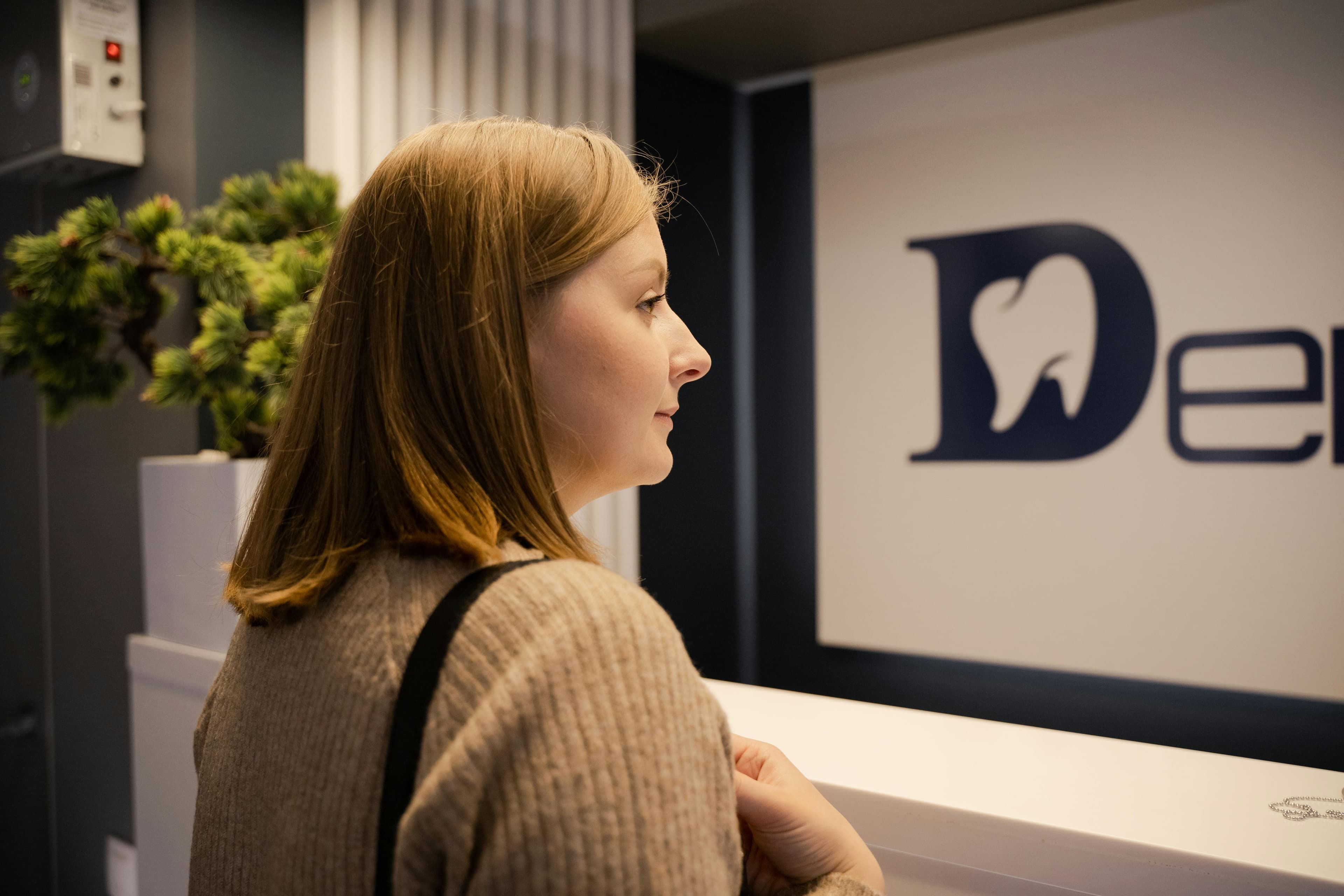 Photo Woman Standing At Dental Reception Desk Looking At Wall Logo Do Dentists Take Walk Ins Signage Visible In Modern Clinic Interior