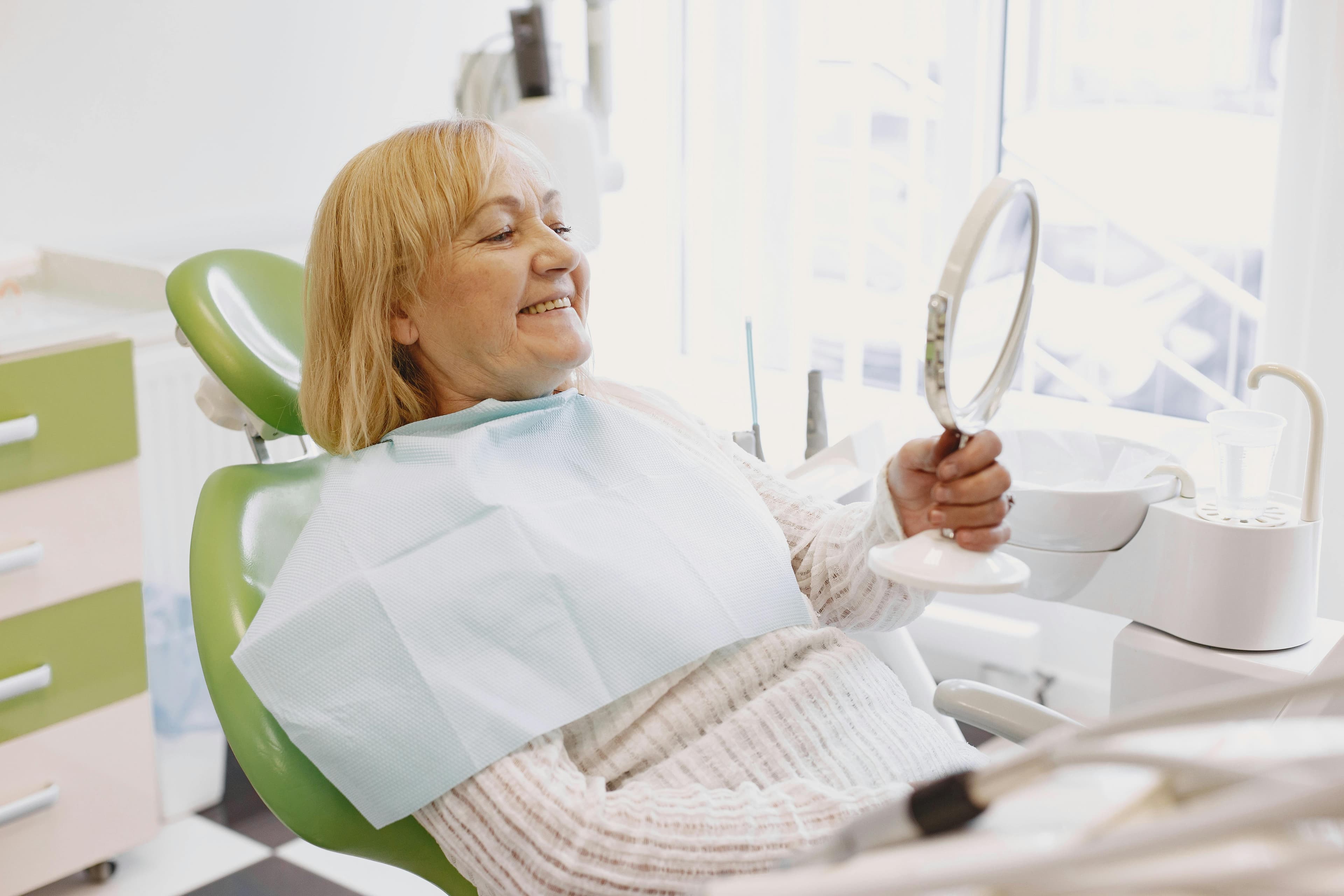 Photo Elderly Woman Smiling In Dental Chair Holding Hand Mirror After Treatment How Long Do Dental Implants Take To Heal Concept