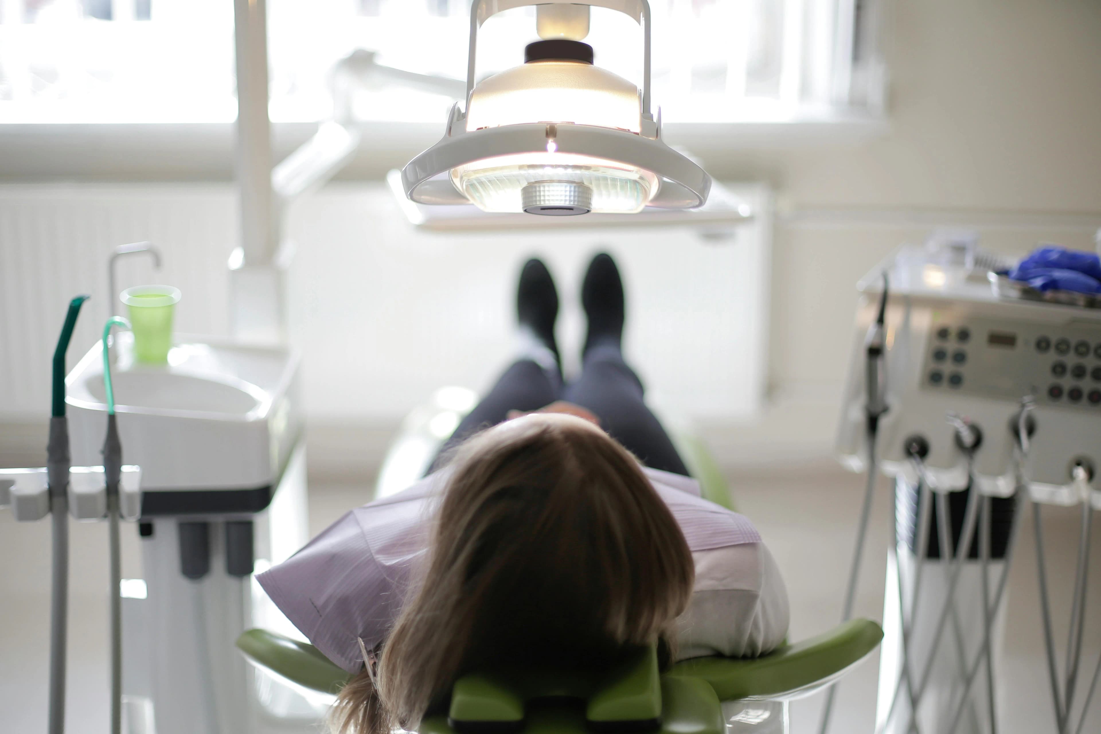 Photo Patient Lying In Dental Chair Under Overhead Light Demonstrating How To Handle Dental Emergency Anxiety During A Clinic Visit