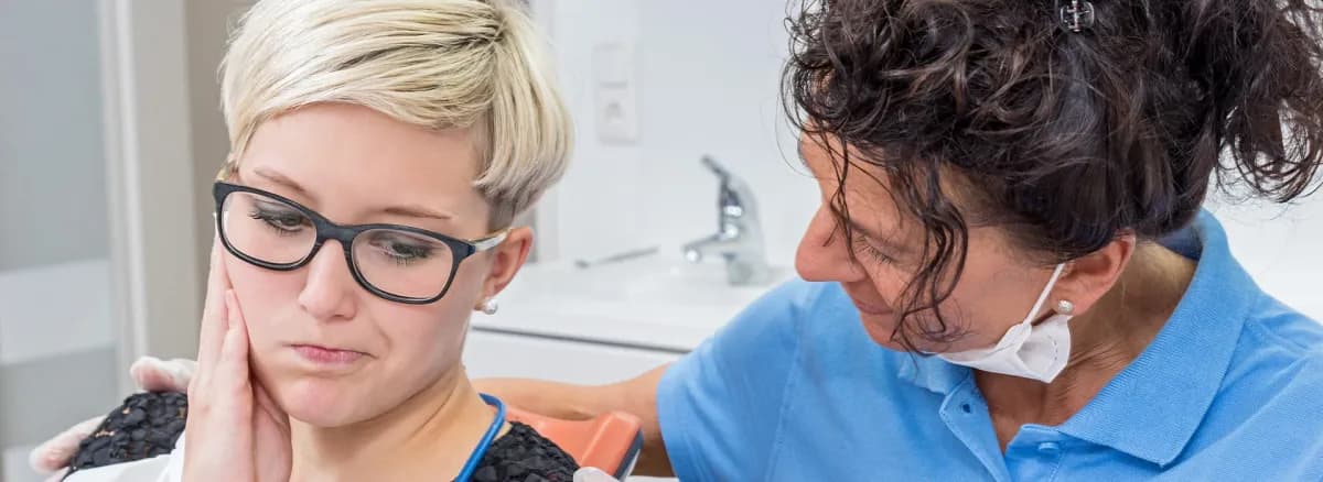 Woman Holding Her Jaw In Pain While Being Consulted By Dental Professional In Blue Uniform Discussing Same Day Dental Implants For Relief