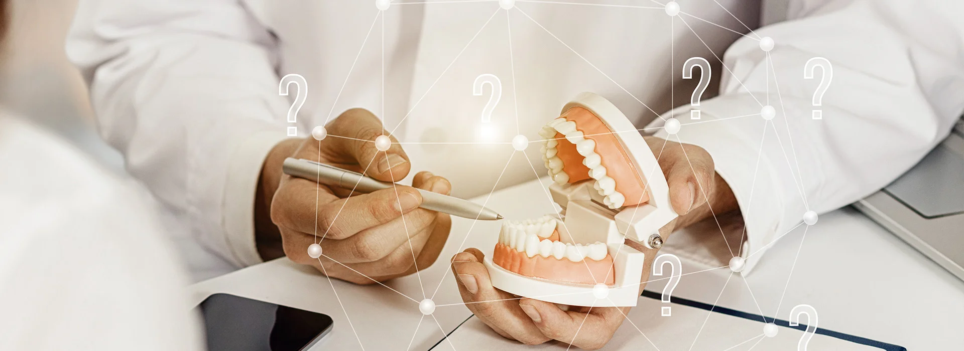 Dentist holding dental model and pen explaining treatment options to patient while discussing how much do dental implants cost with question mark graphics overlaid.