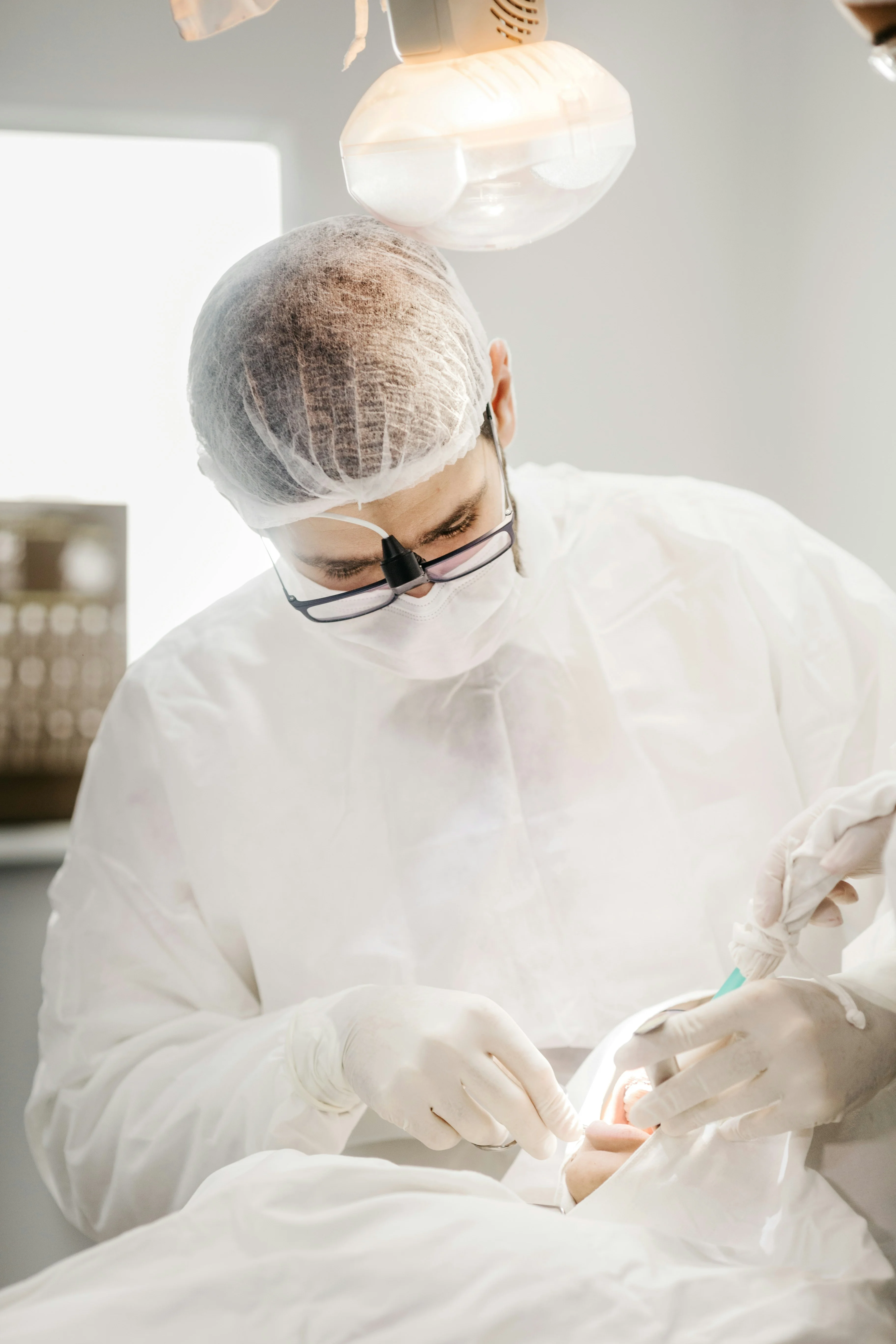 Dentist in white protective gear performing procedure on patient demonstrating situations of what qualifies as a dental emergency in clinical setting.
    