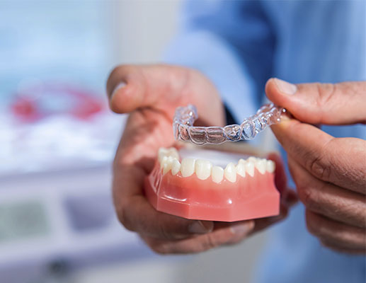 Hands holding clear aligner above dental model to show straightening process while considering if is Invisalign cheaper than braces for treatment options.