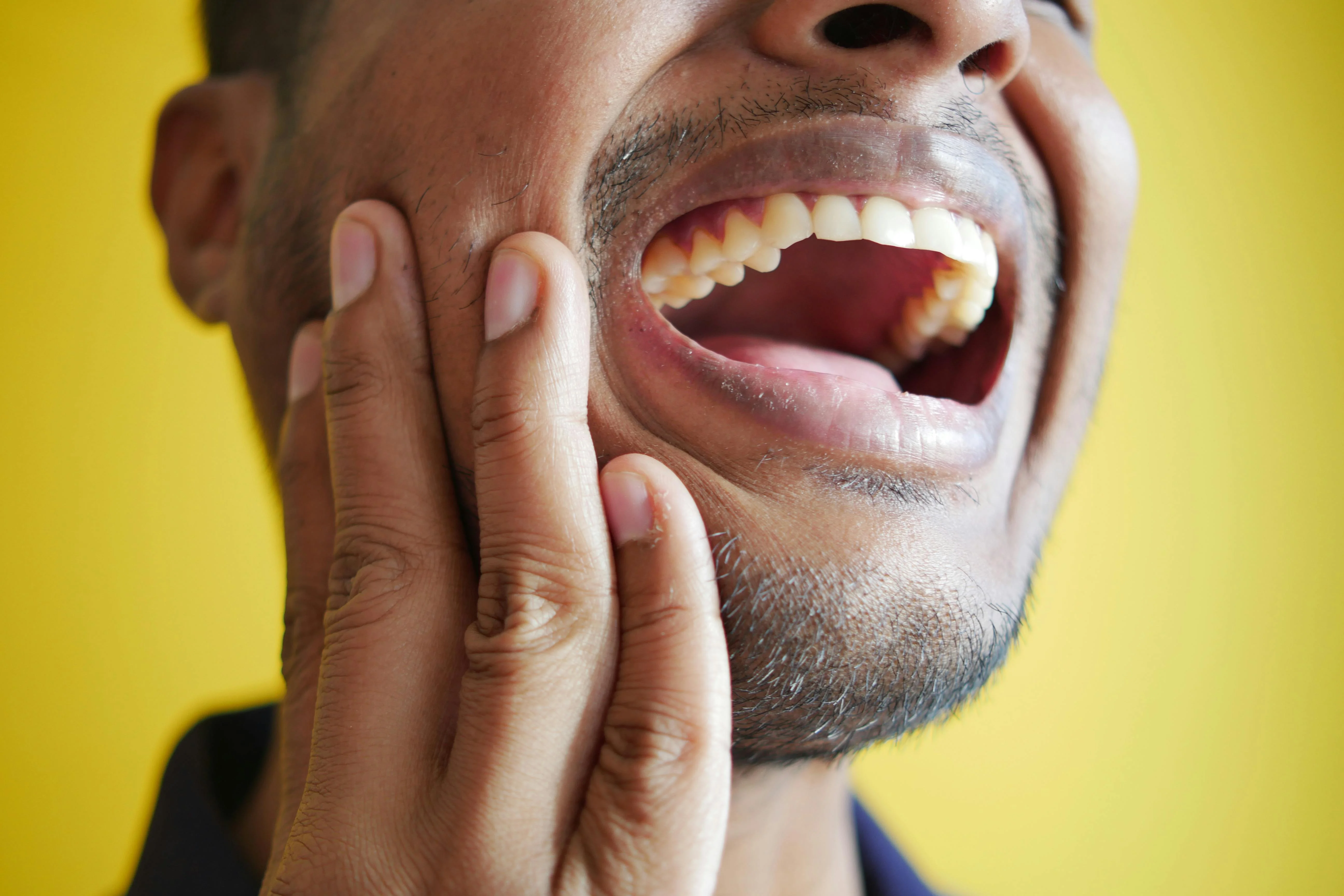 Man holding his jaw in pain with mouth open showing visible discomfort as one of the dental emergency examples related to severe tooth infection or abscess.