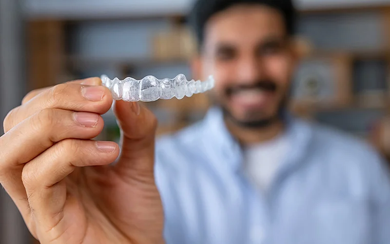 What are Invisalign aligners made of? - Man holding clear Invisalign aligner with smile in background.