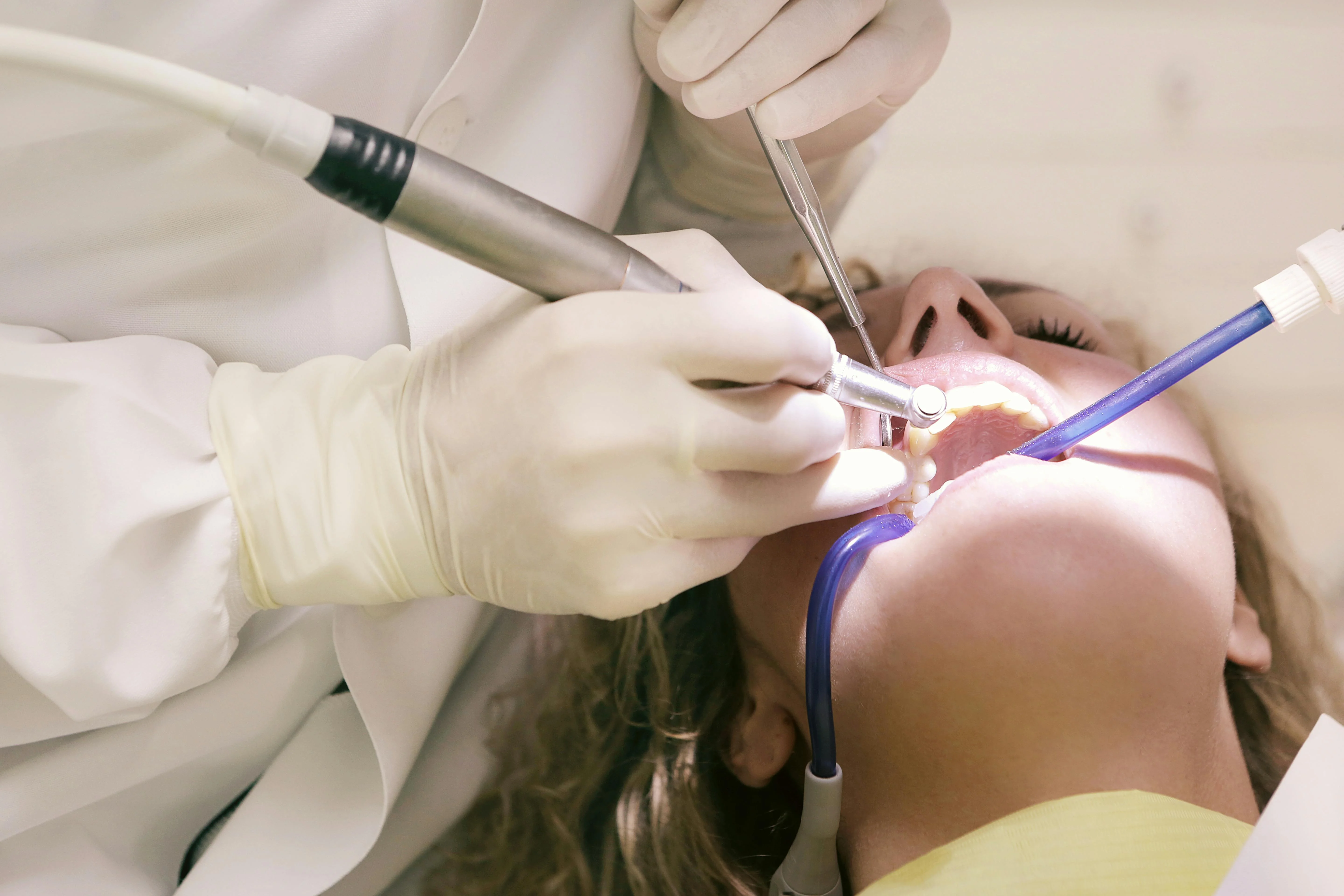 What is preventive dentistry - close up of dentist in white coat using dental drill and tools on patient with suction tube during oral procedure.
    
