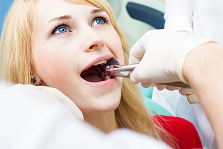 Woman in red shirt receiving tooth extraction from dentist wearing gloves thinking does full extraction cure gum disease.