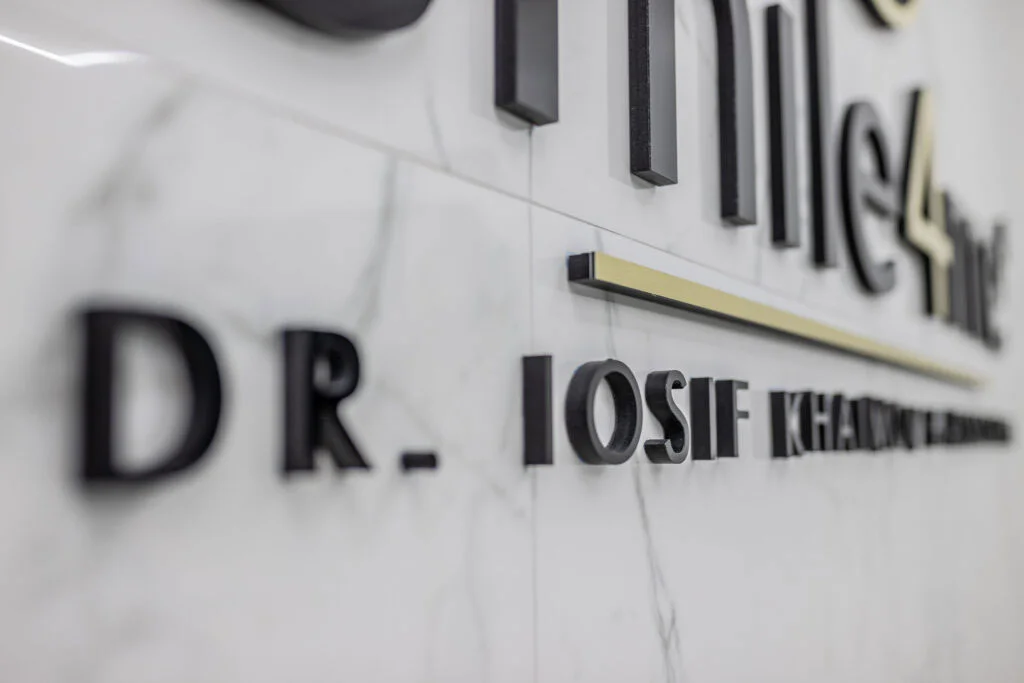 Close up of 3D letter signage on marble wall inside dental office displaying name Dr. Iosif Khaimov at Smile4Me Dental Care.