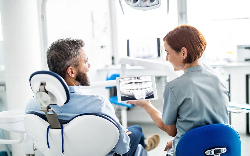 Dentist showing digital X-ray to smiling male patient during consultation to discuss treatment options like all on 6 dental implants in modern clinic