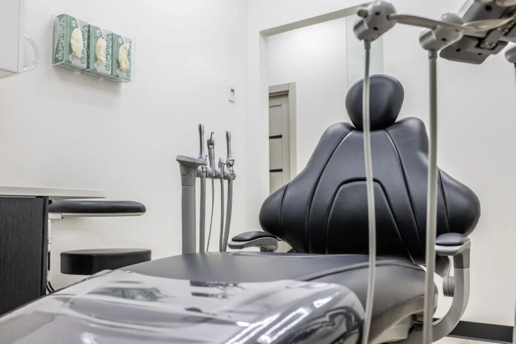 Modern dental room with black patient chair, white walls, dental tools on stand, and stools arranged for dental treatment session.